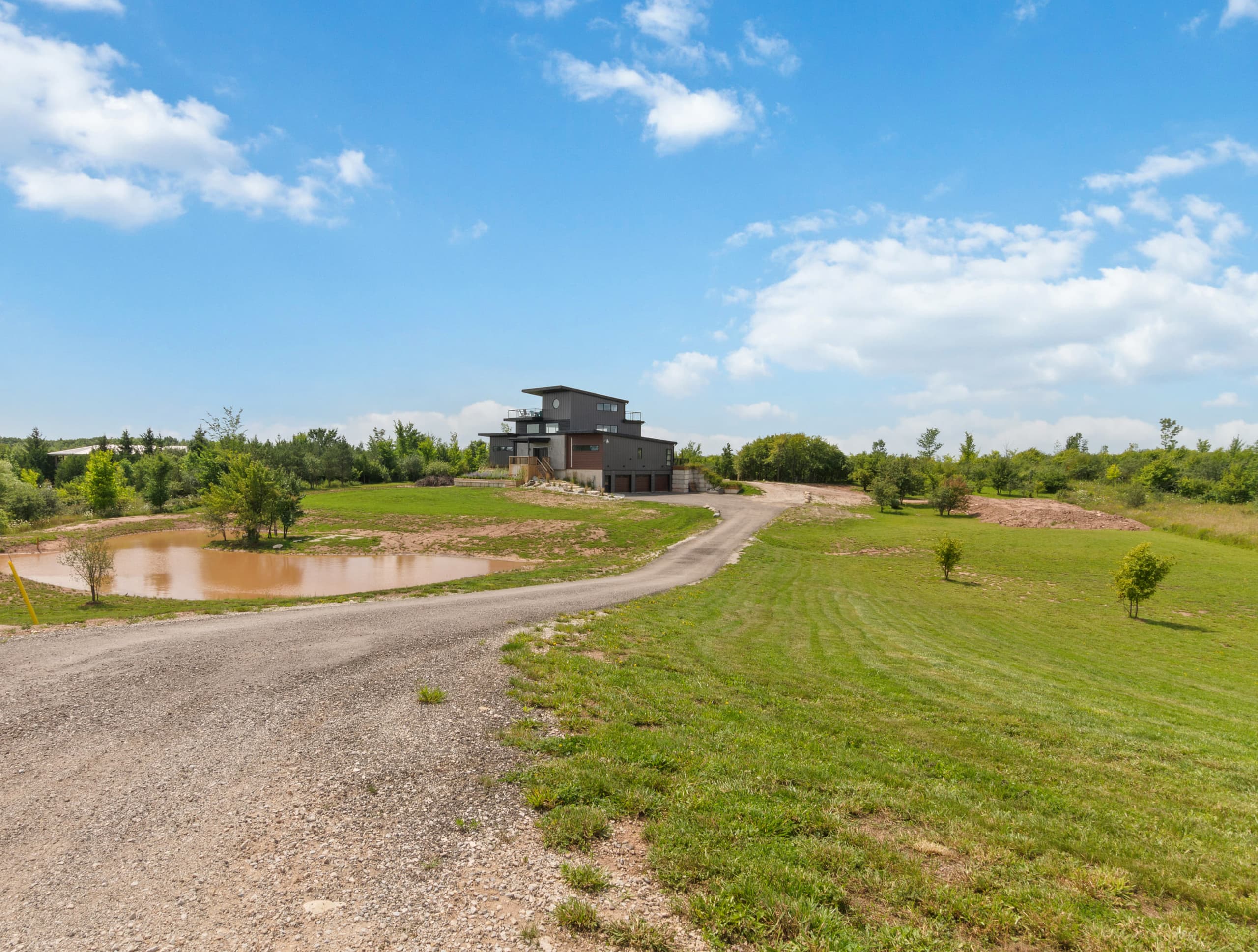 A gravel drive curving past a pond and open mown fields toward the house on a rise